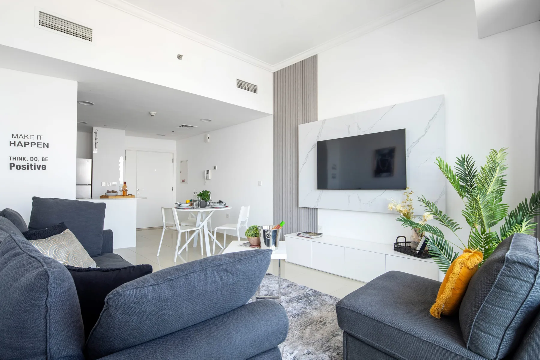 A bright living room with blue seating, a dining table, and a wall-mounted television.
