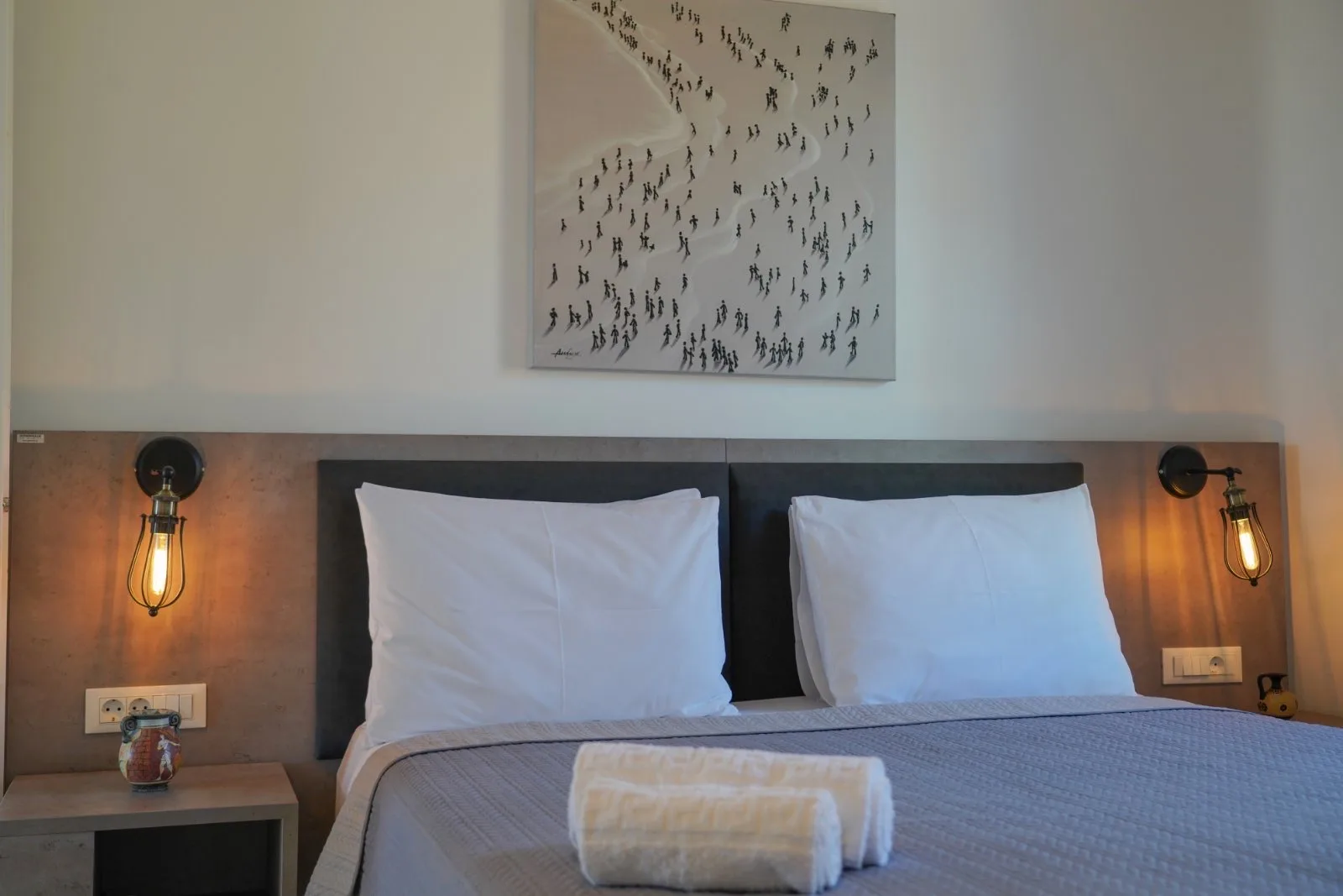 A bedroom with a neatly made bed and framed artwork above it.