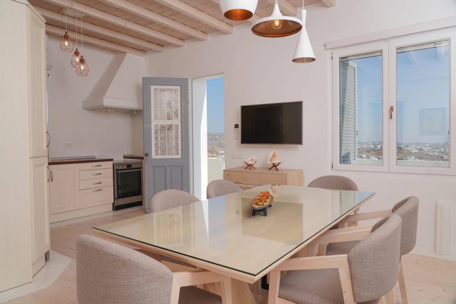 A bright dining area with a glass table beside the kitchen and large windows.