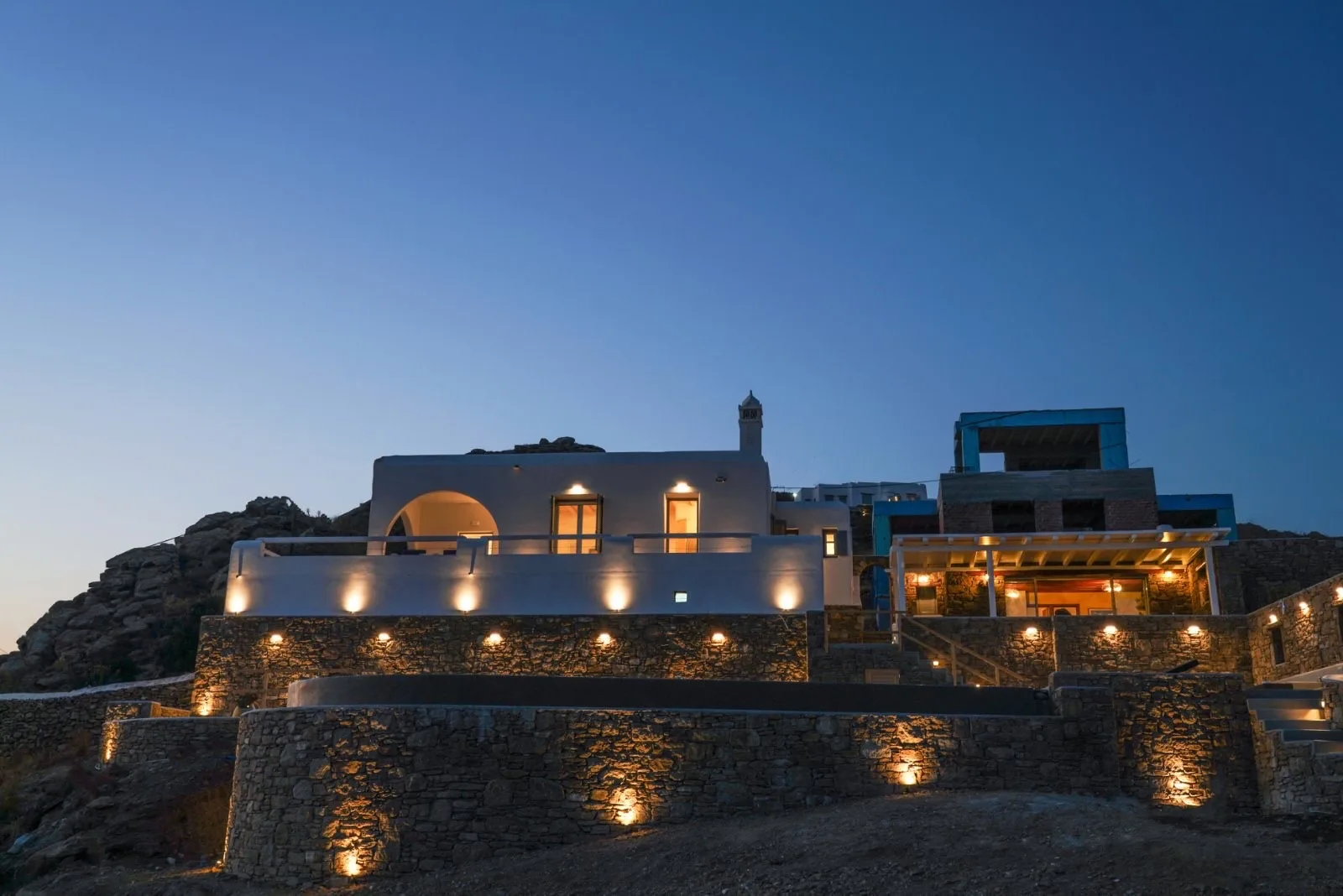 A modern hillside villa glows with warm exterior lighting at dusk.