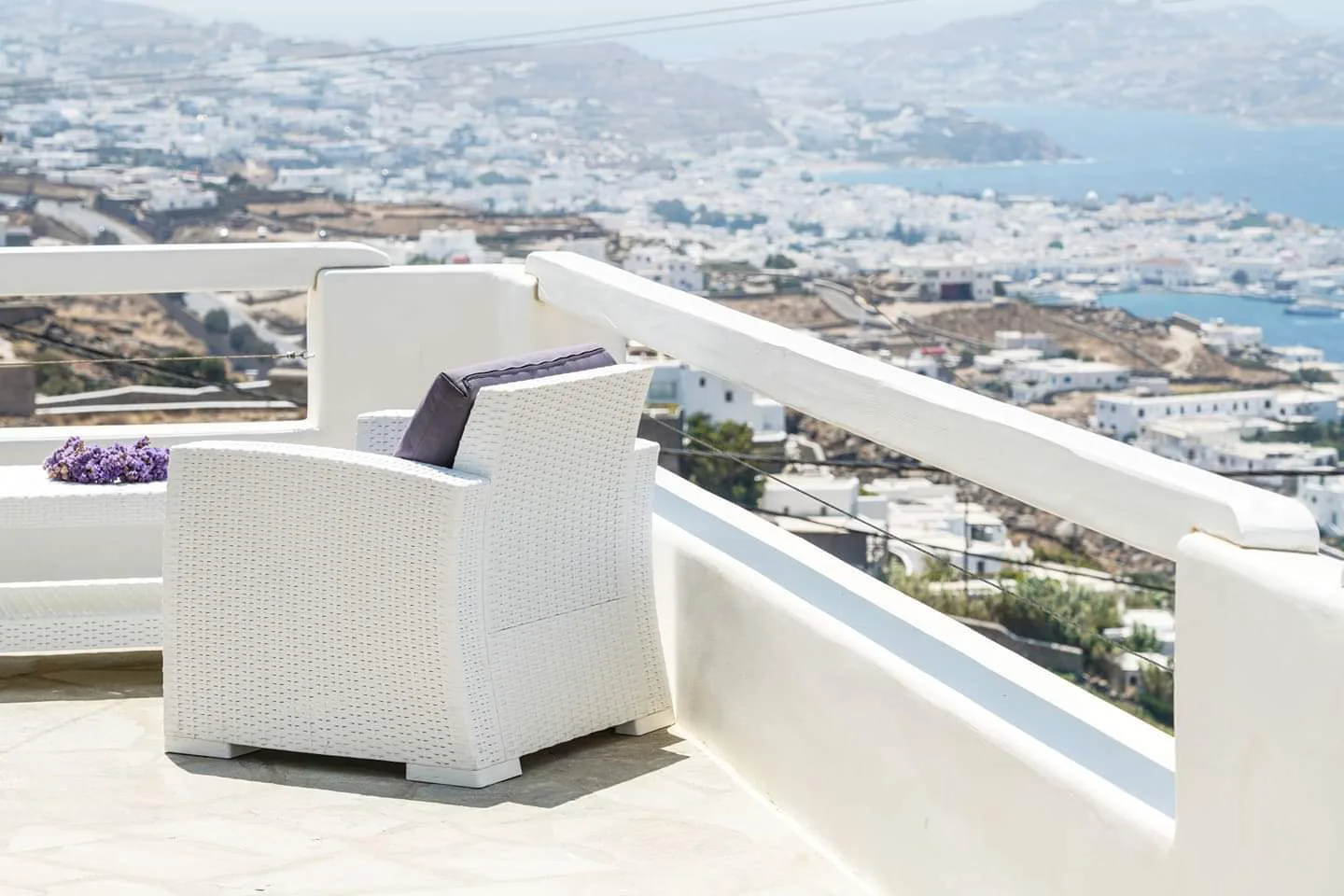 A white terrace seating area overlooks a coastal town and the sea.