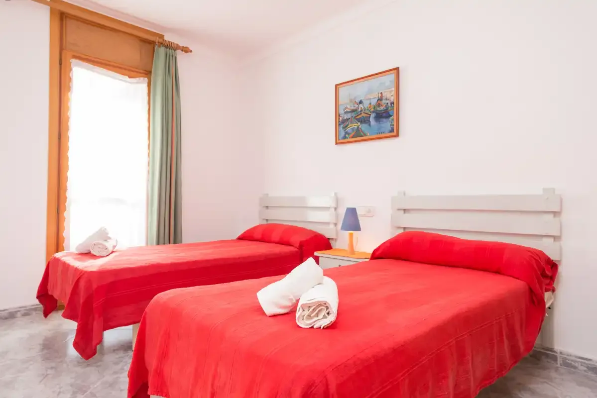 A bedroom with two beds covered in red bedspreads and a window.