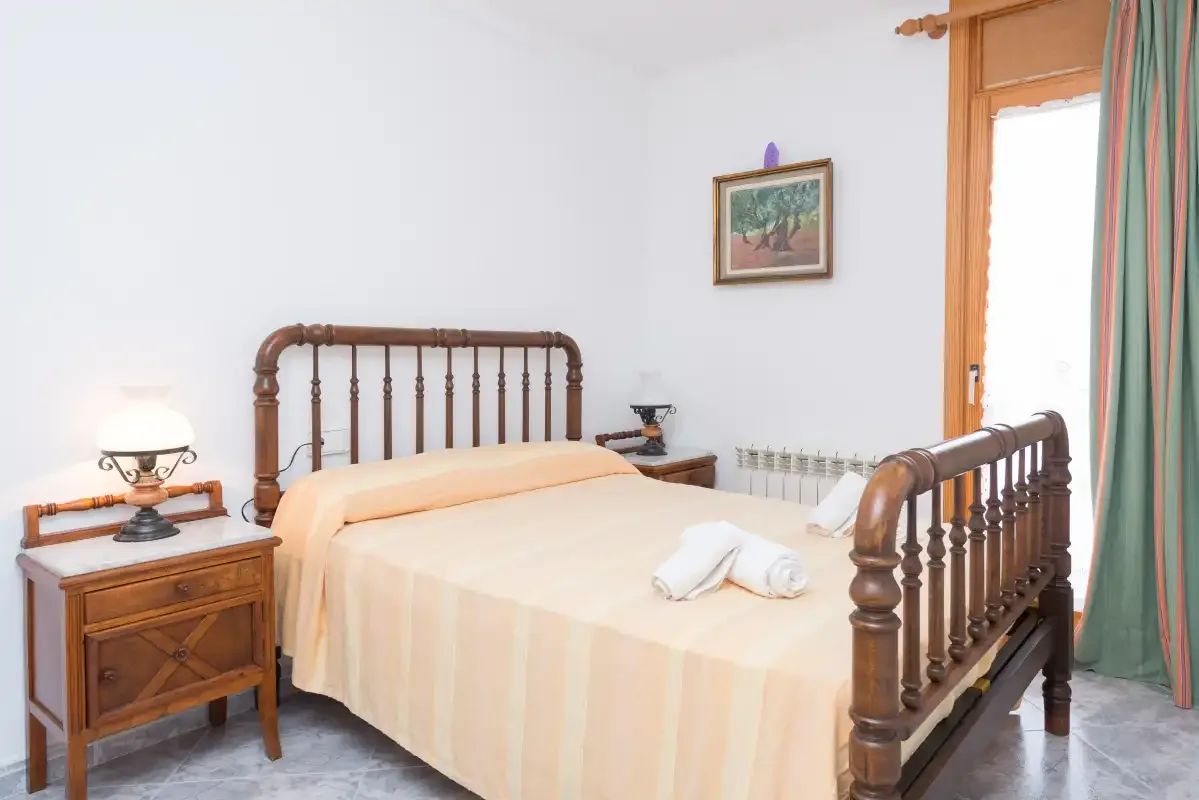 A bedroom with a wooden bed, bedside table, and window.