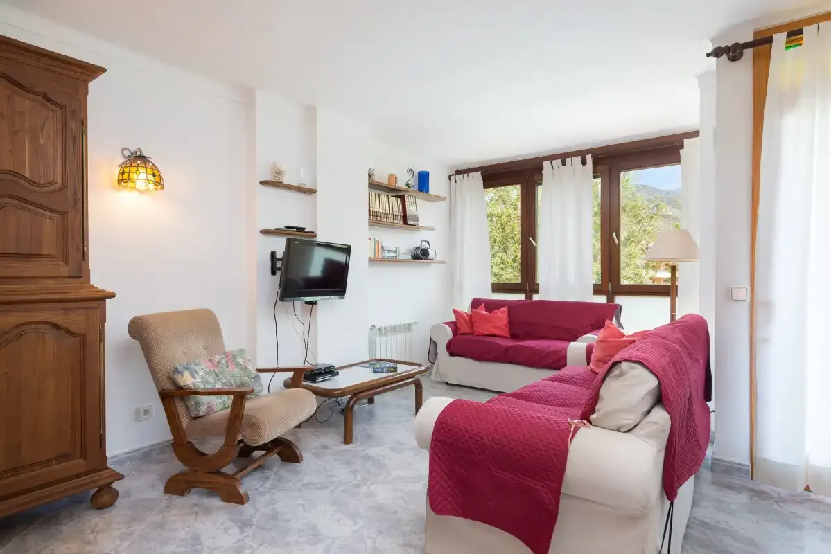 A living room with seating, a television, and large windows.
