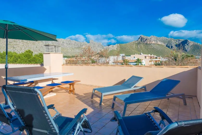 A sunny rooftop terrace with blue lounge chairs and mountain views.