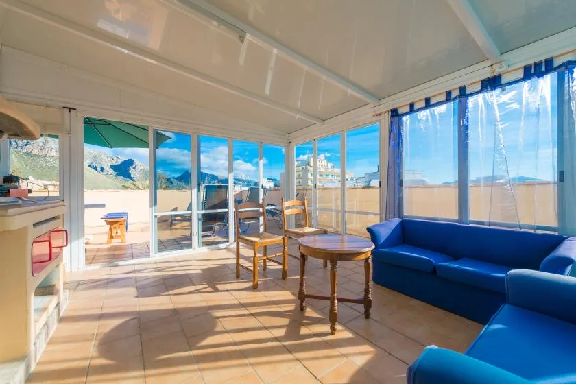 A bright enclosed patio with blue seating and glass doors opening onto a sunny outdoor area.