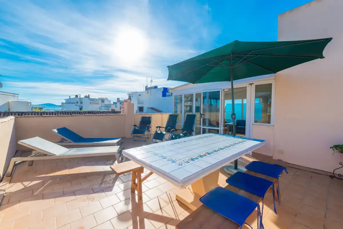 A sunny rooftop terrace with a dining table, seating, and a large shade umbrella.