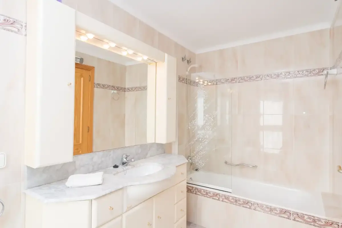 A bathroom with a vanity, mirror, and bathtub with a glass screen.
