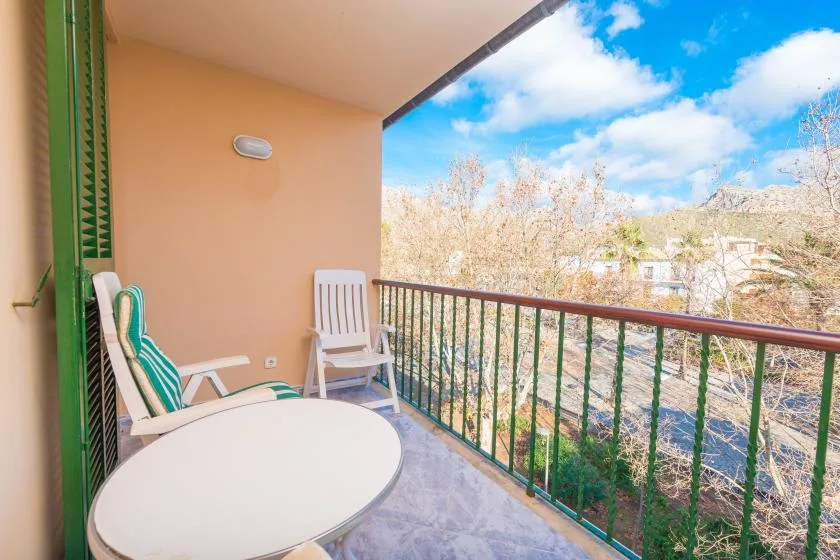 A covered balcony has seating and a round table overlooking trees.