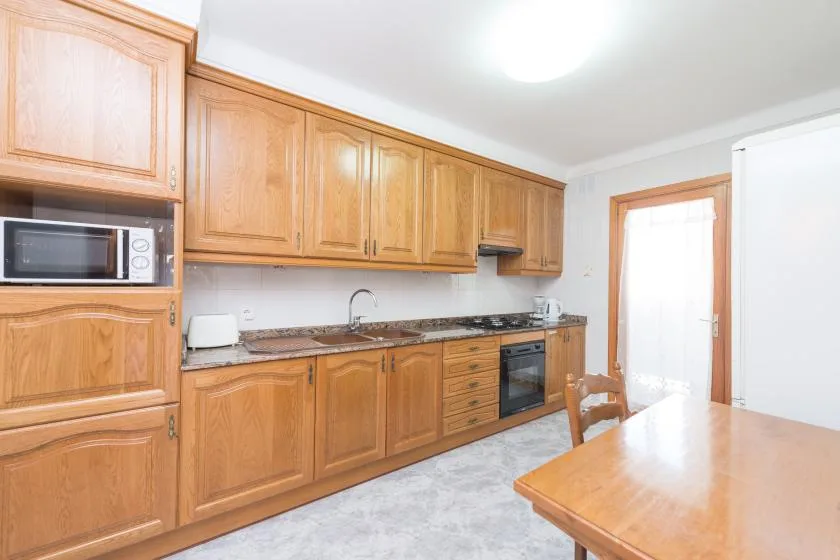 A bright kitchen with wooden cabinets, a counter, and a dining table.