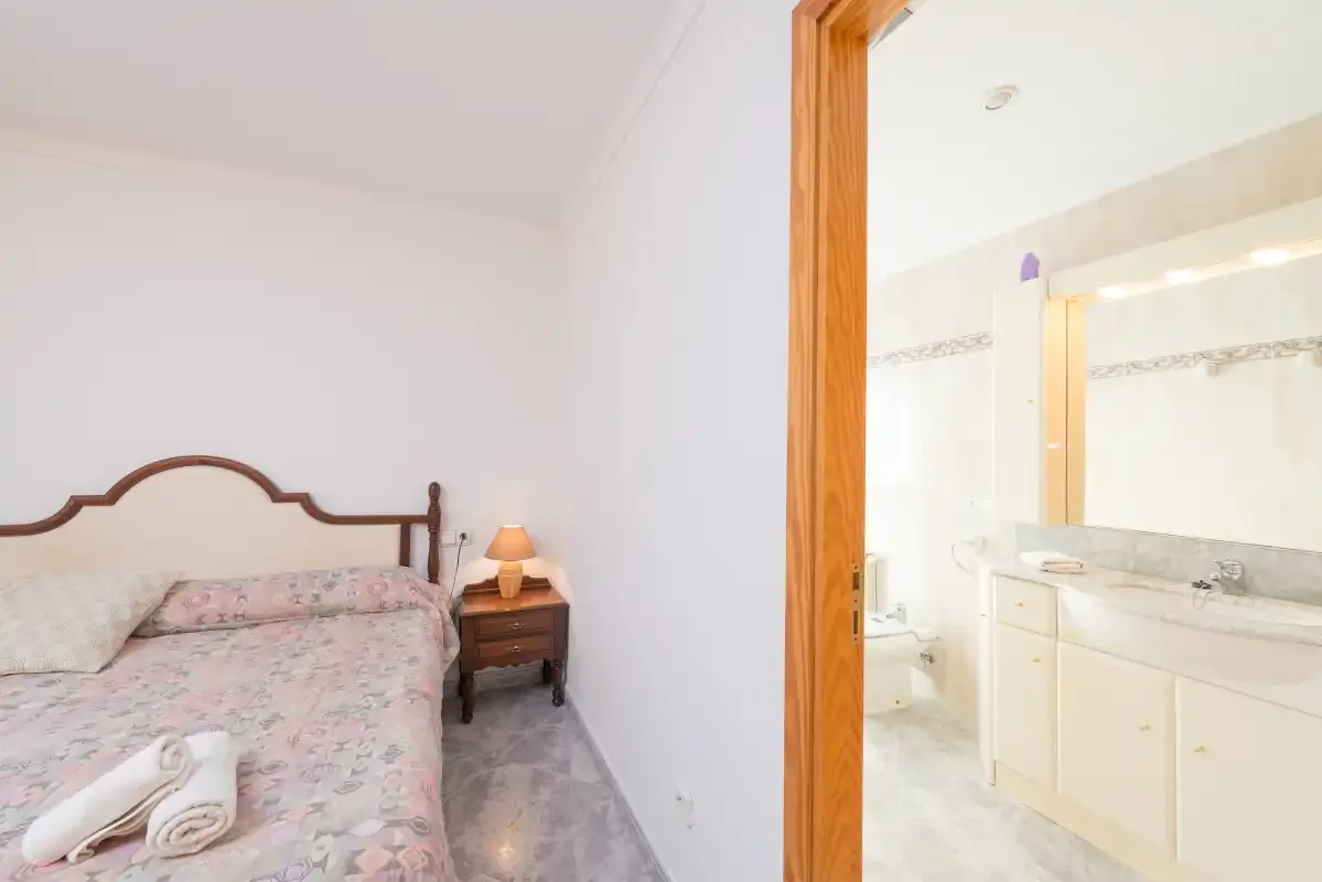 A bedroom with a floral bedspread opens onto a bathroom vanity.