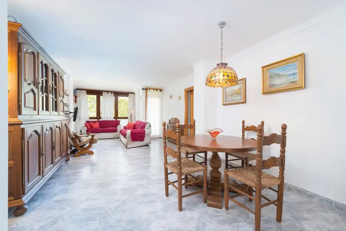 A dining area with wooden seating opens onto a living space with a bright pink sofa.