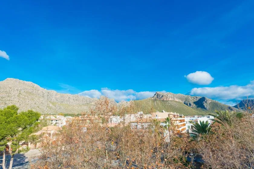 A mountain landscape rises behind buildings and trees under a clear blue sky.
