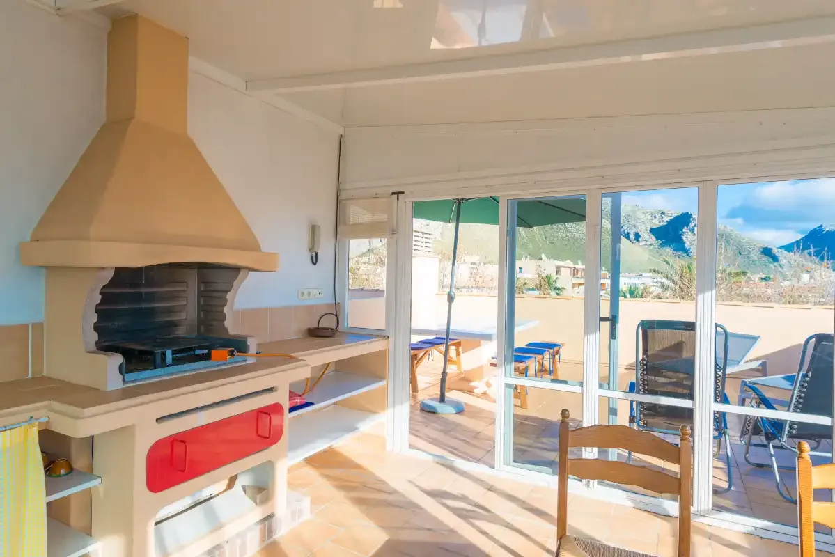 A bright indoor barbecue area opens onto a terrace through glass doors.