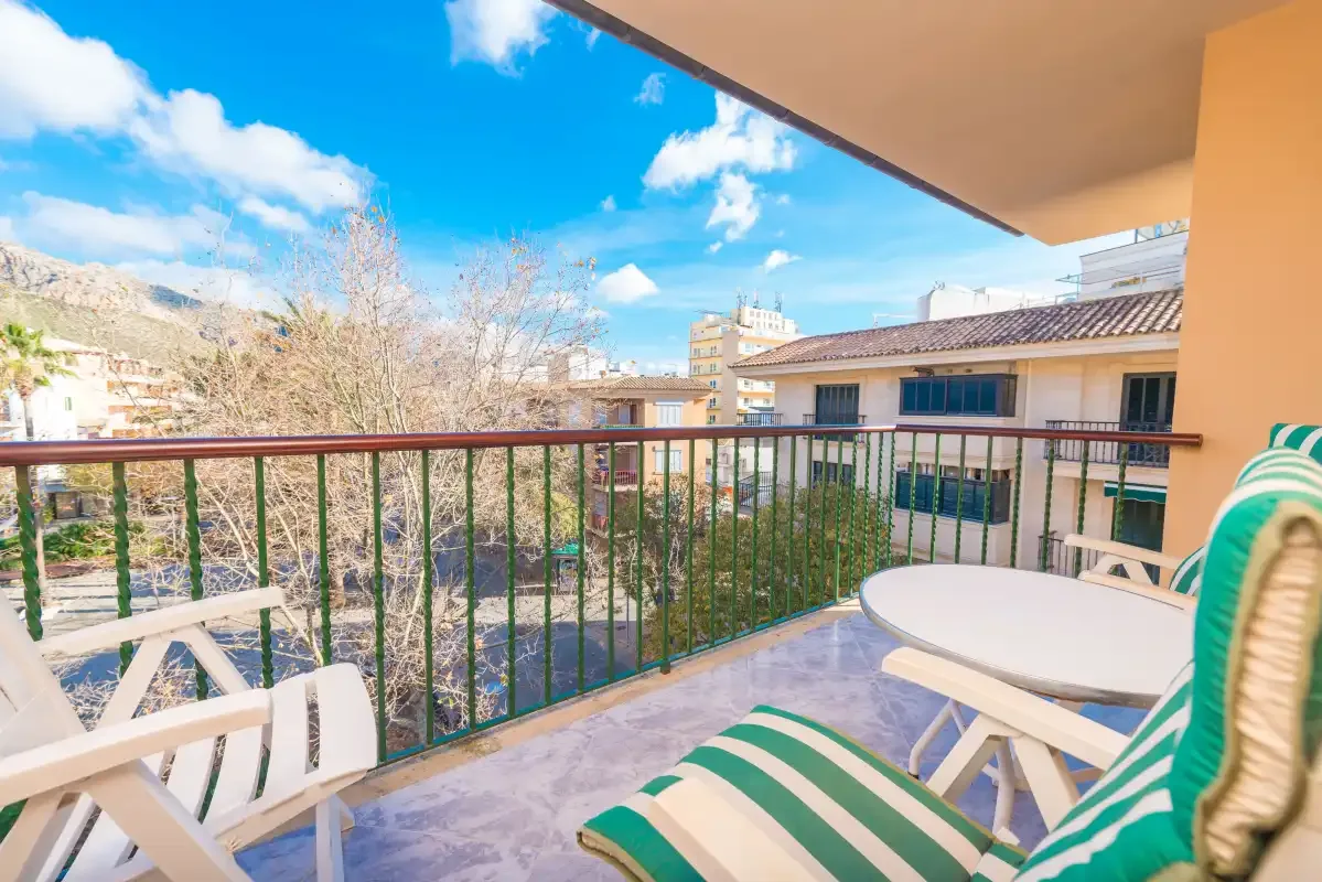 A balcony with striped seating and a view of nearby buildings and hills.