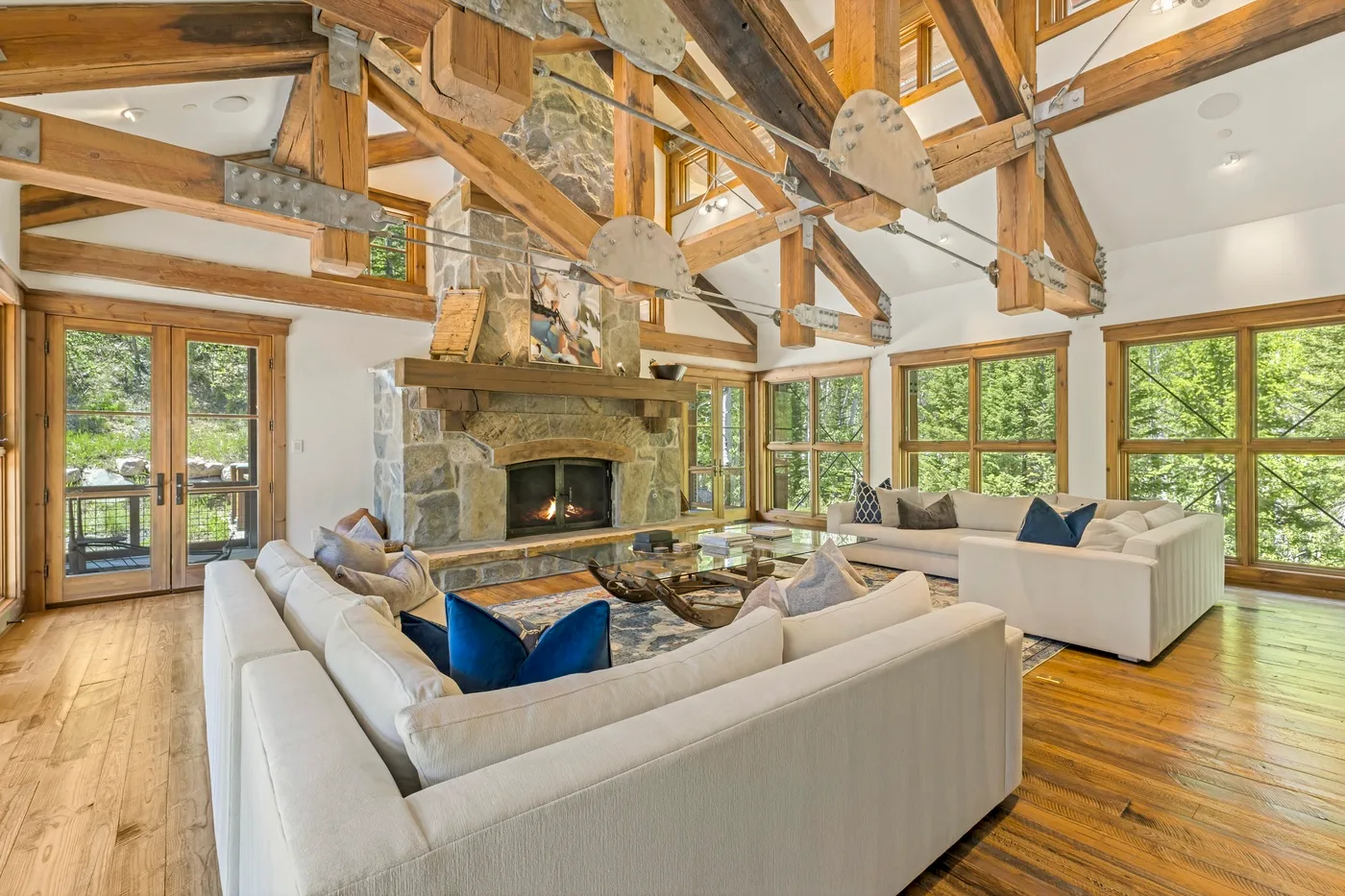 A spacious living room with seating around a stone fireplace and large windows.