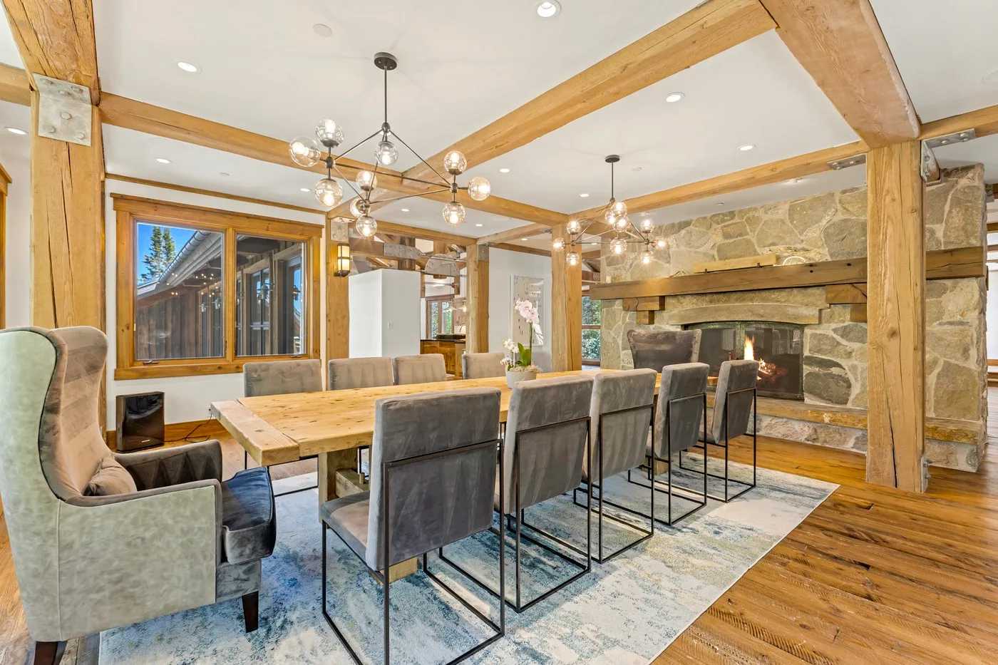 A dining area with a long table and upholstered seating beside a stone fireplace.
