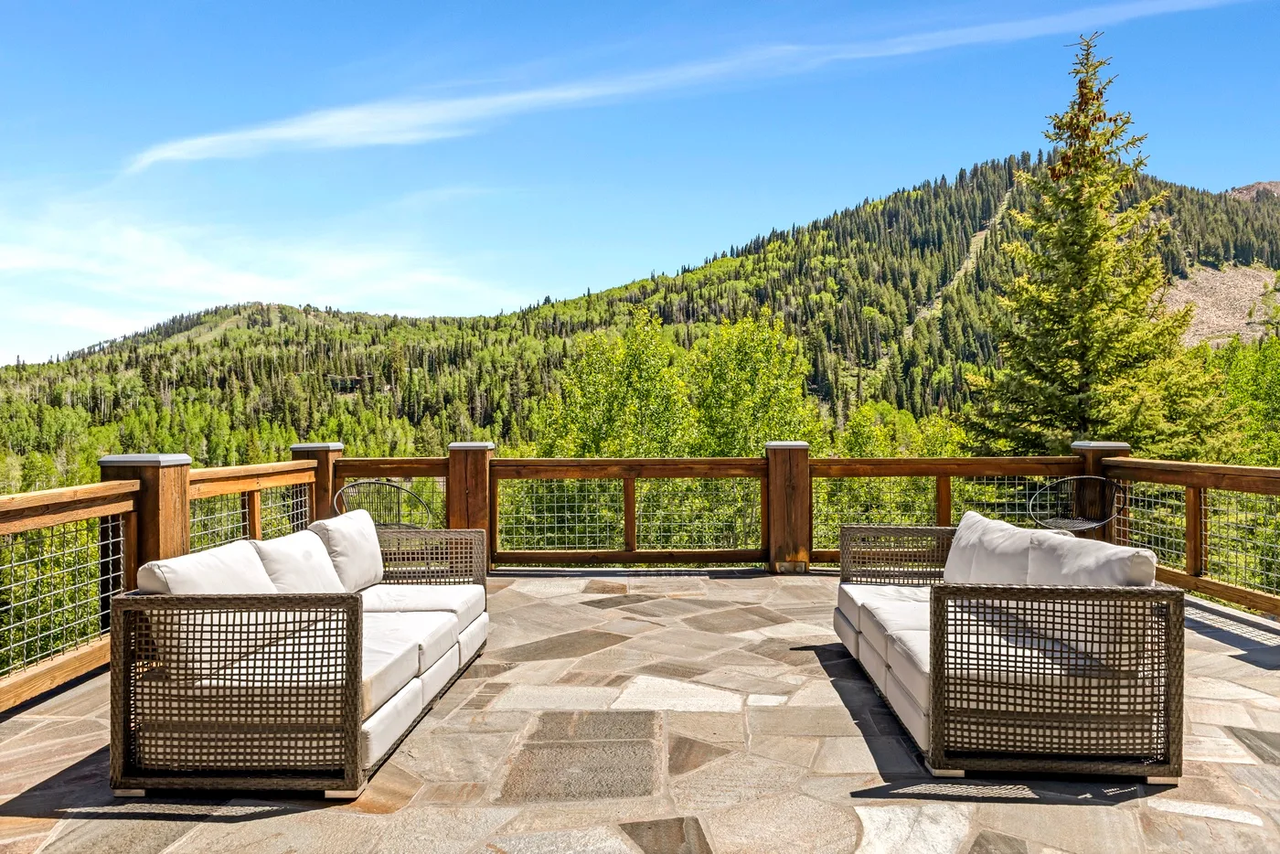 An outdoor terrace has seating and a railing overlooking a forested mountain.