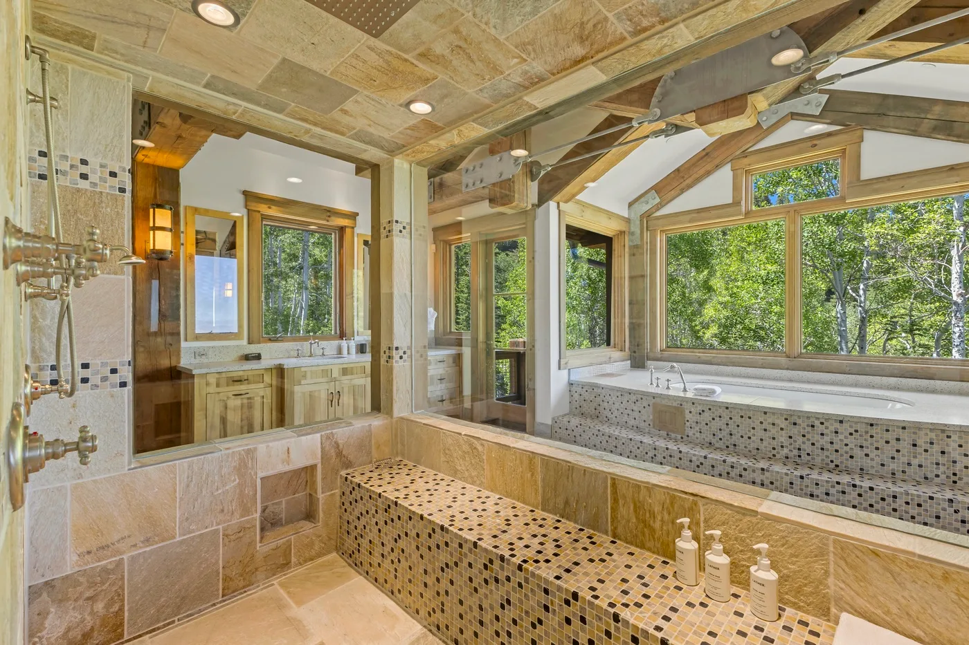 A tiled bathroom with a long built-in tub beneath large windows.