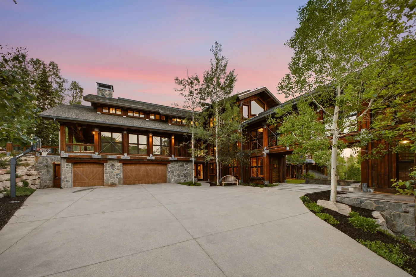 A large house with a broad paved driveway and trees under a pink evening sky.