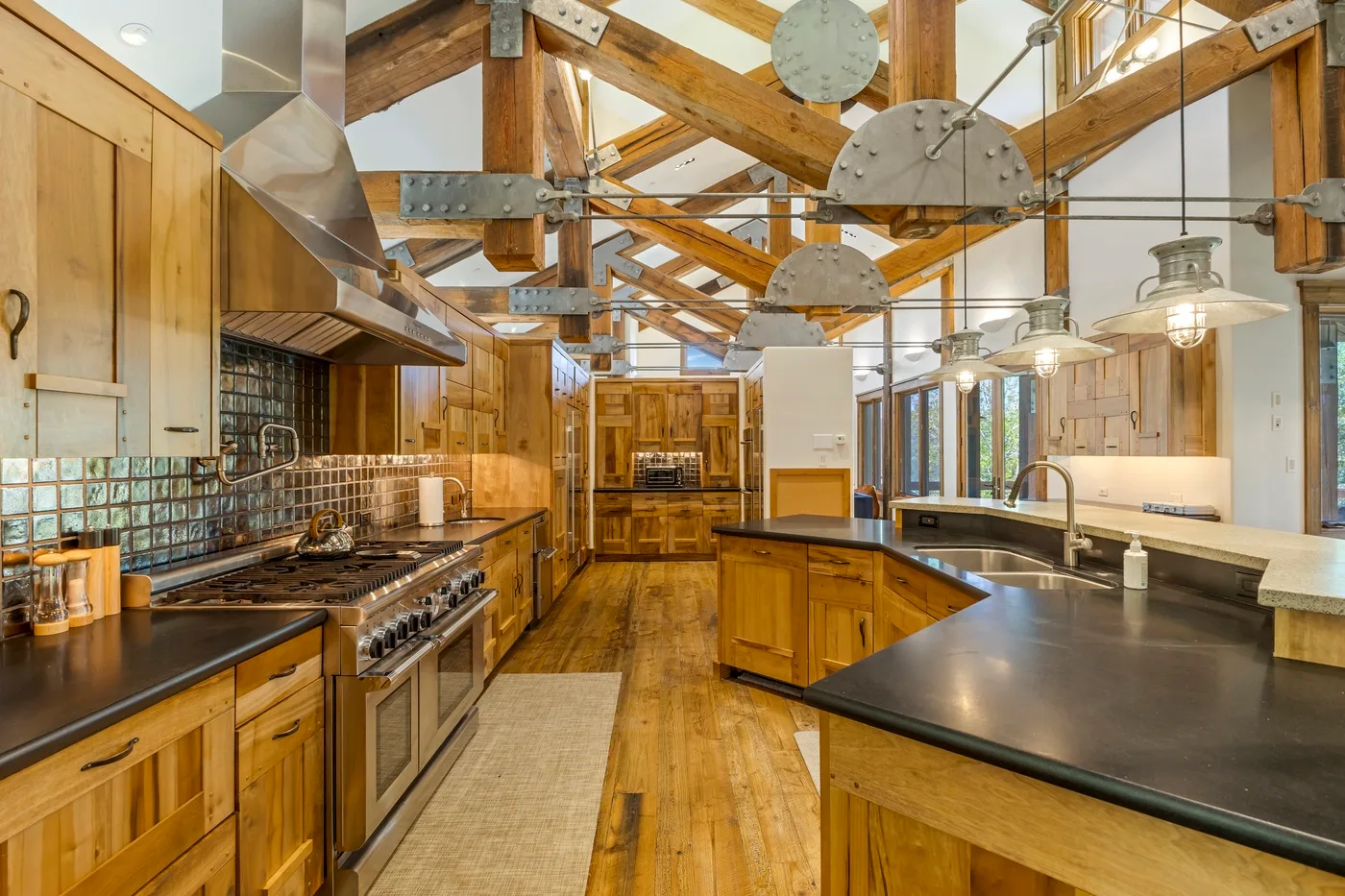 A spacious kitchen with wooden cabinetry, dark counters, and exposed timber beams.