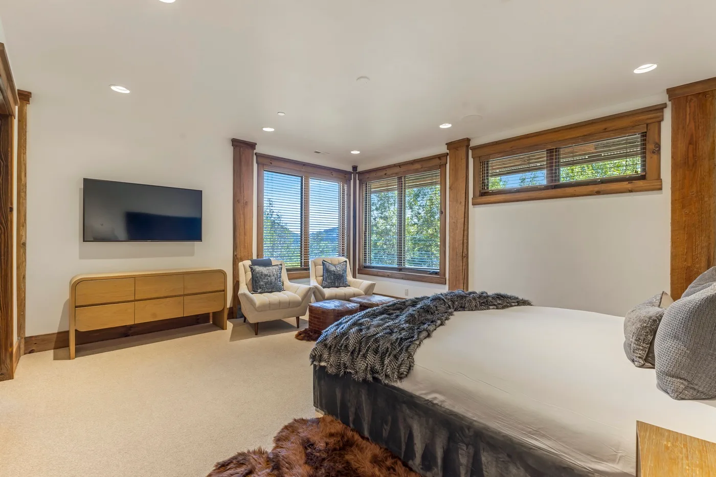 A bedroom with a bed, seating, and windows overlooking trees.