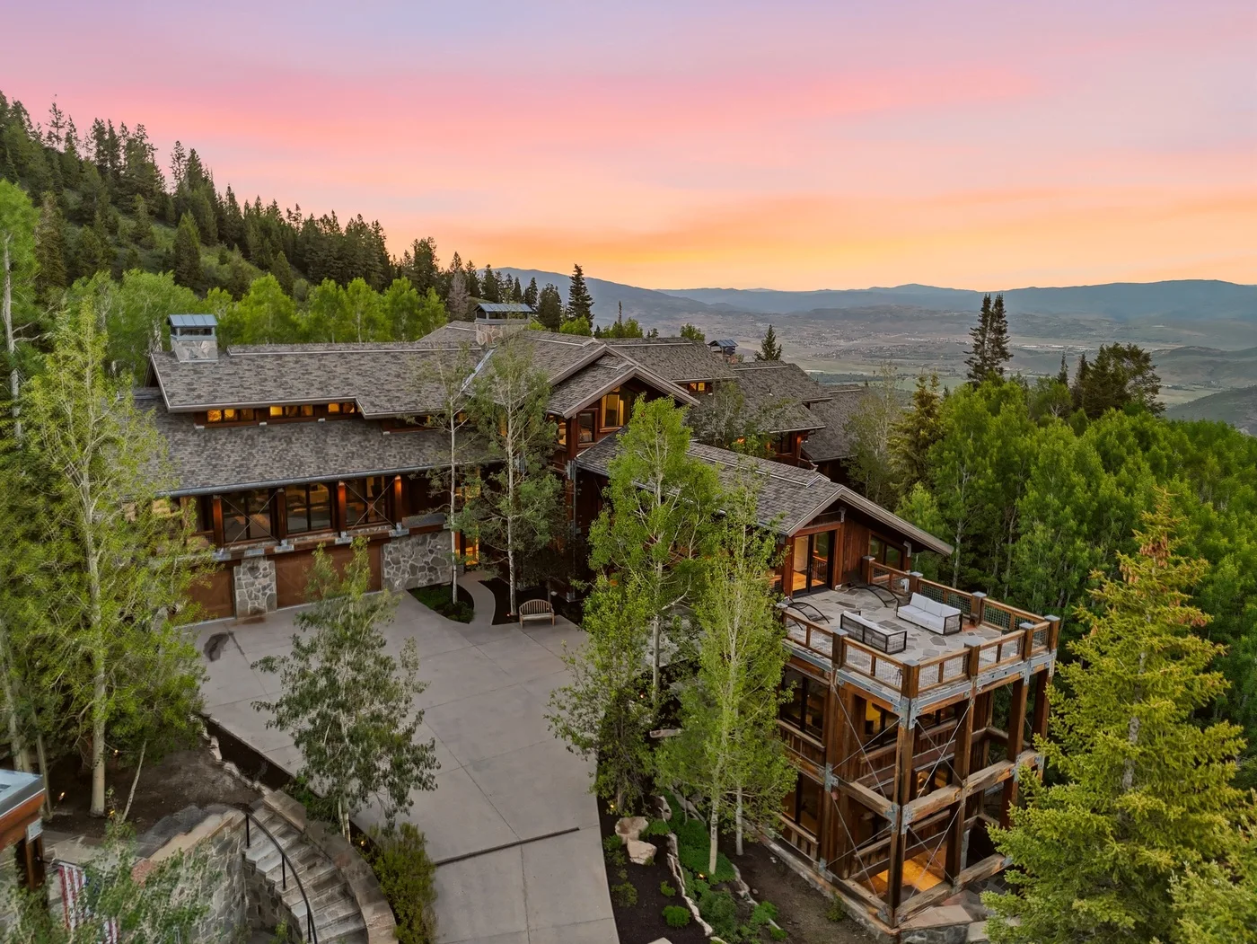 A mountain lodge complex sits among trees above a broad valley at sunset.