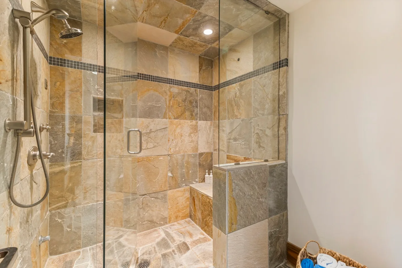 A tiled bathroom shower with a handheld showerhead and glass panels.