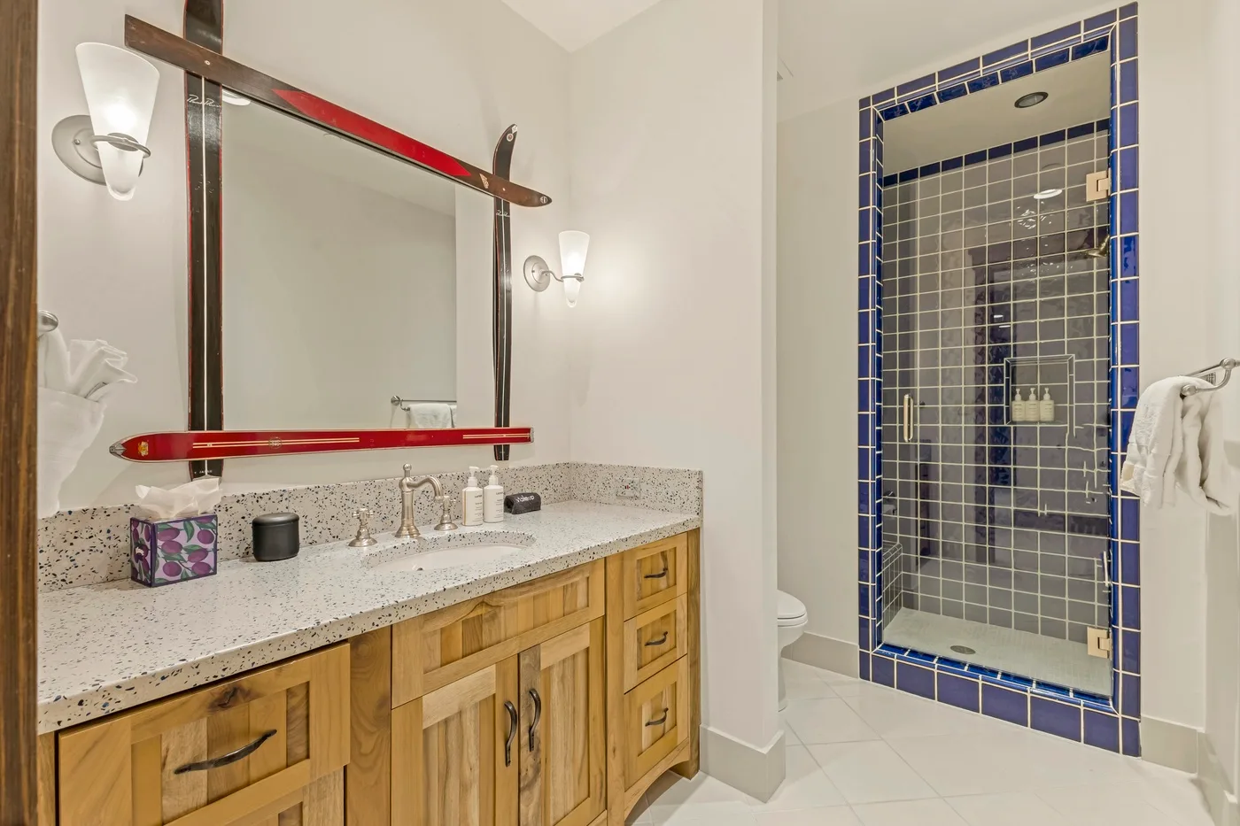 A bathroom vanity with a large mirror stands beside a tiled shower.
