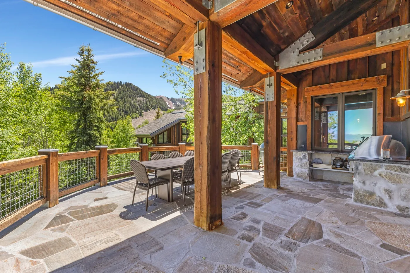 A covered outdoor dining area with timber beams overlooks a wooded hillside.