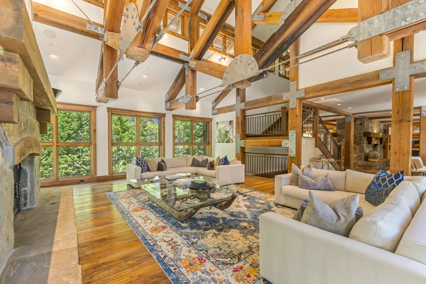 A spacious living room with large windows, exposed wooden beams, and seating around a glass coffee table.