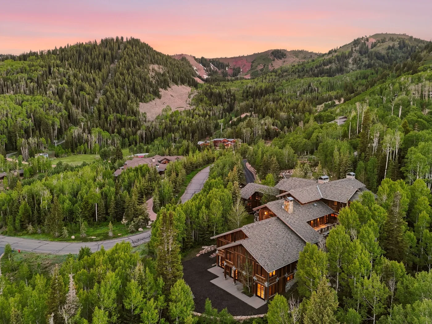 A lodge sits among forested hills beneath a pink evening sky.