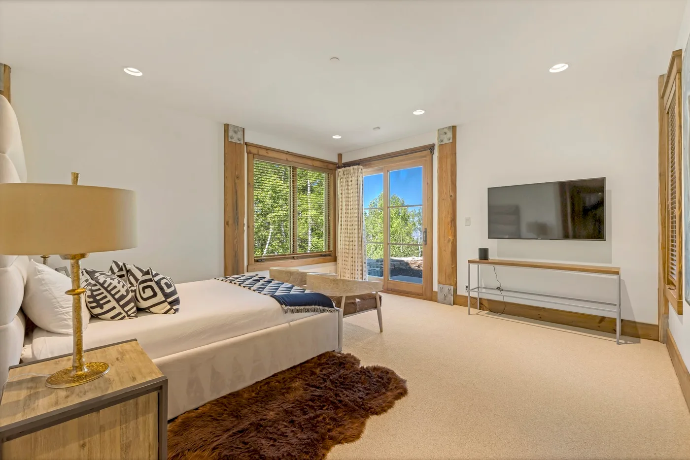 Bedroom with a large bed, television, and windows overlooking greenery.