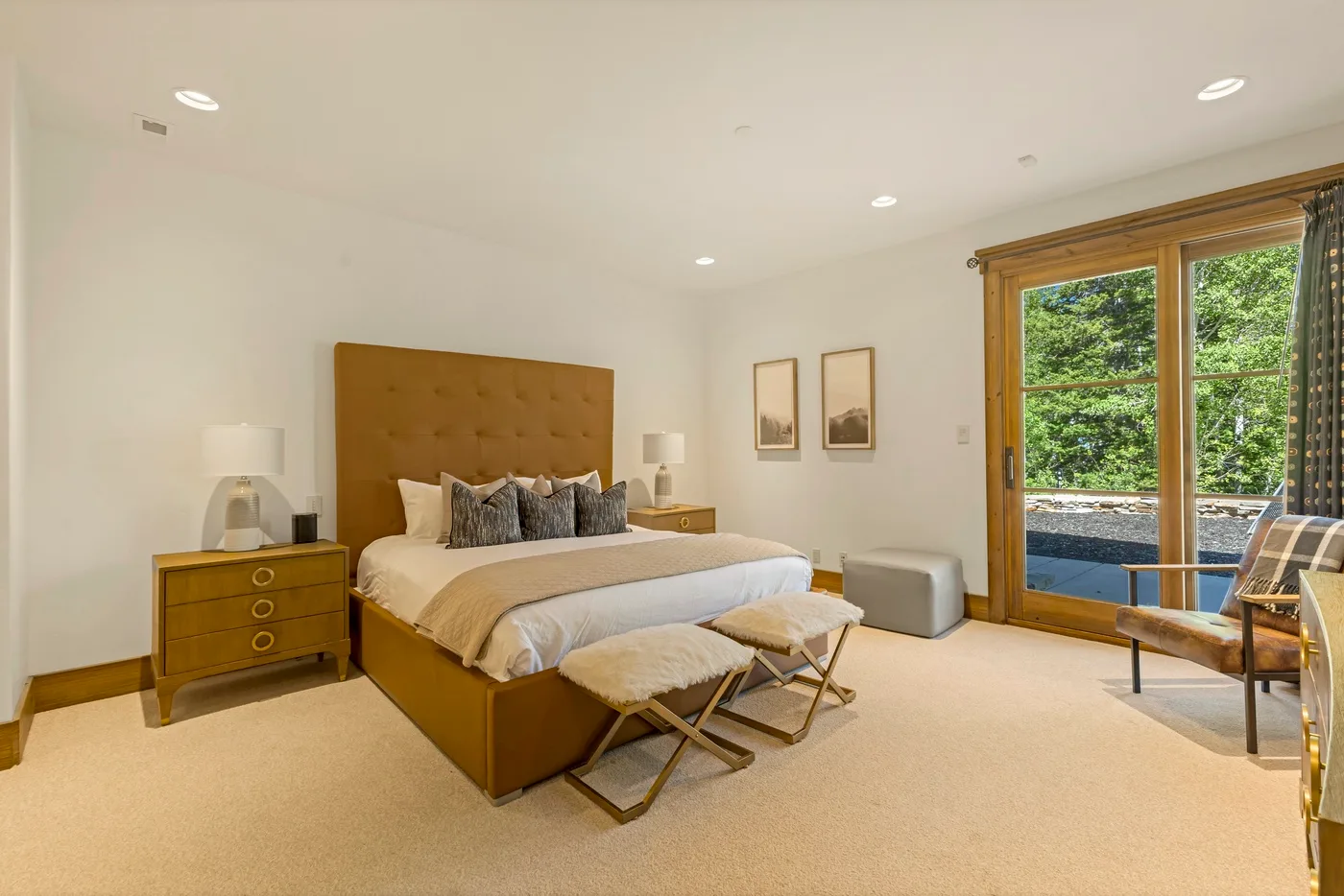 A bright bedroom with a bed, bedside tables, and large windows overlooking greenery.