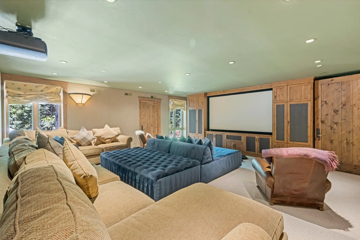 A spacious living room with sectional seating, a large ottoman, and a wall-mounted projection screen.