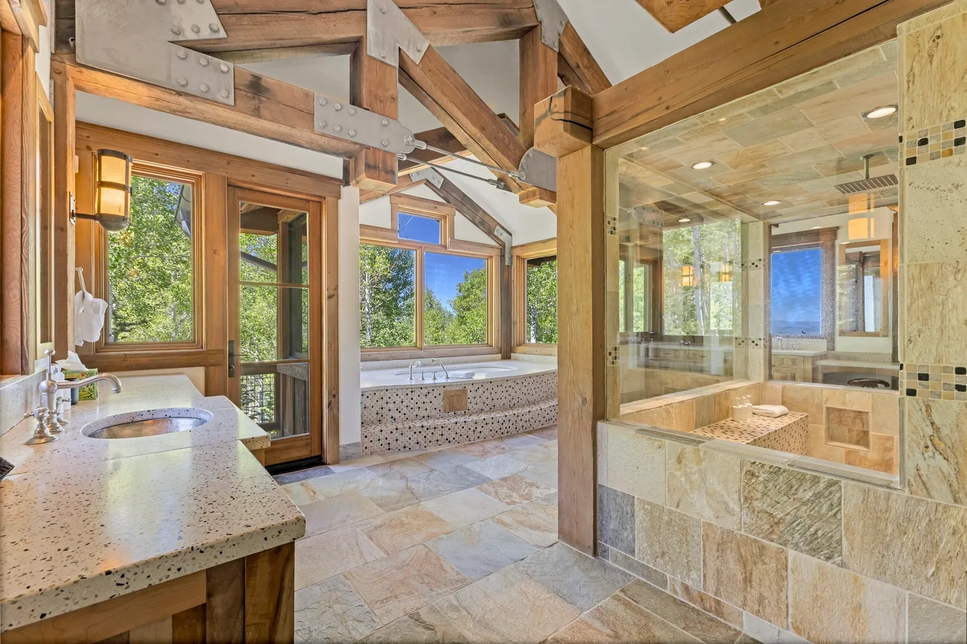 A bright bathroom with a bathtub beneath large windows and a glass shower.