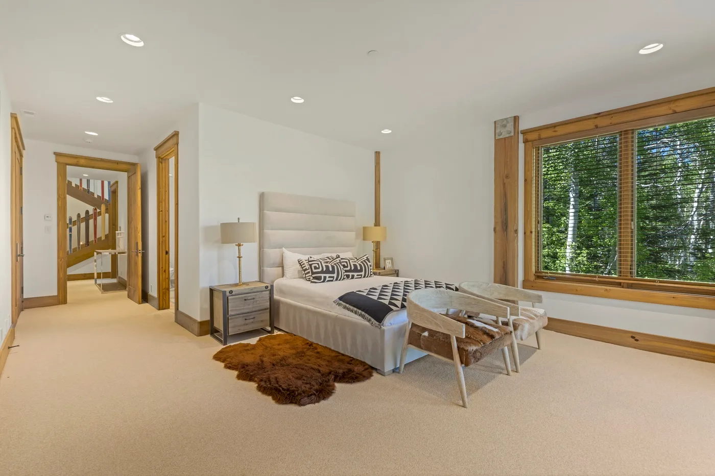A bedroom with a bed, bedside tables, and a large window overlooking greenery.