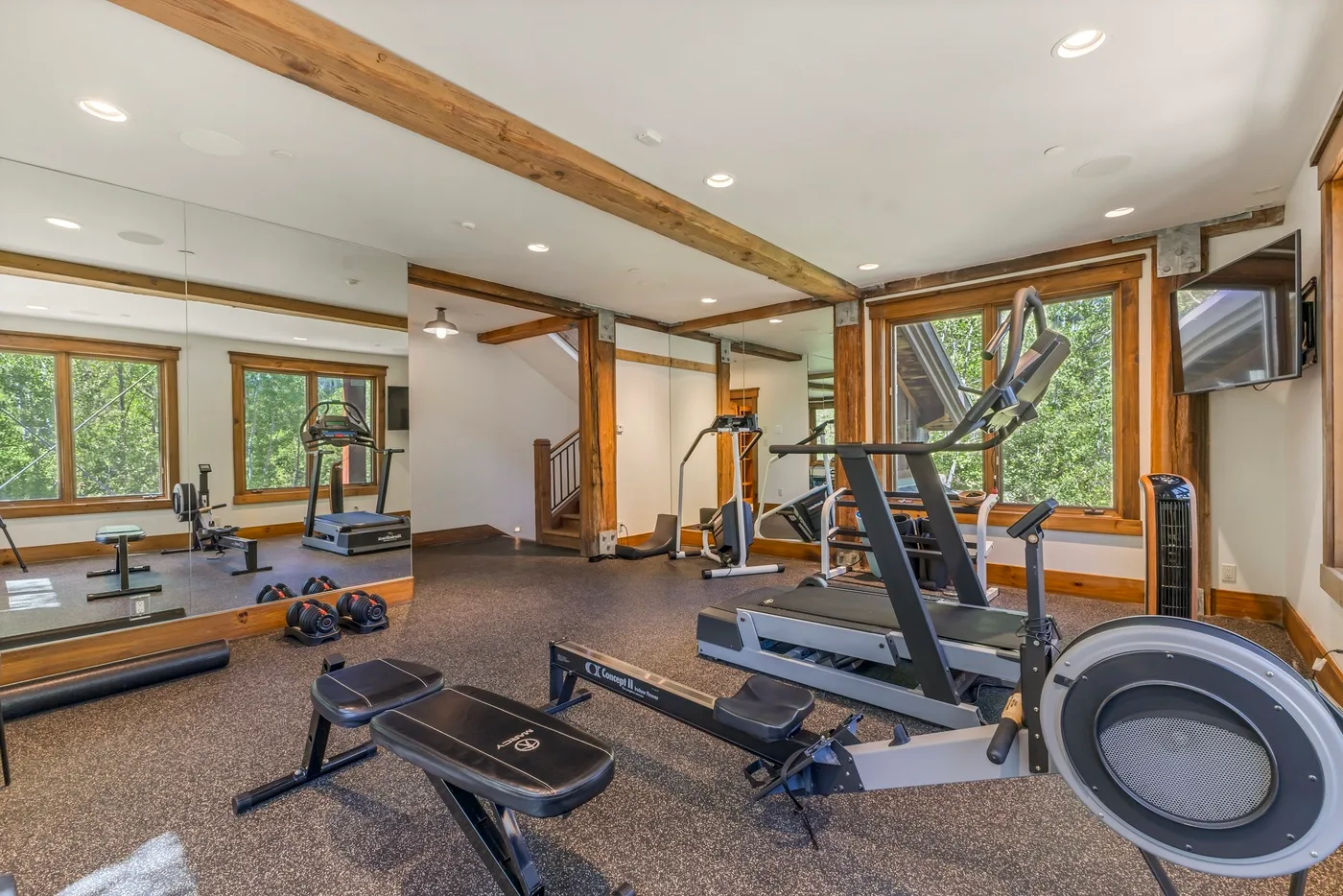 A home gym with exercise machines, weights, and large windows.
