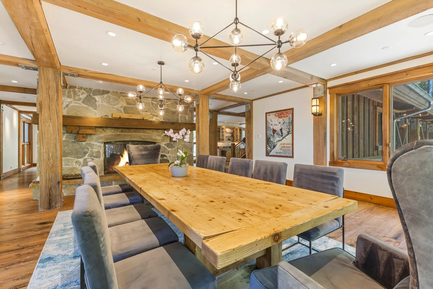 A dining area features a long wooden table, upholstered seating, and a stone fireplace.