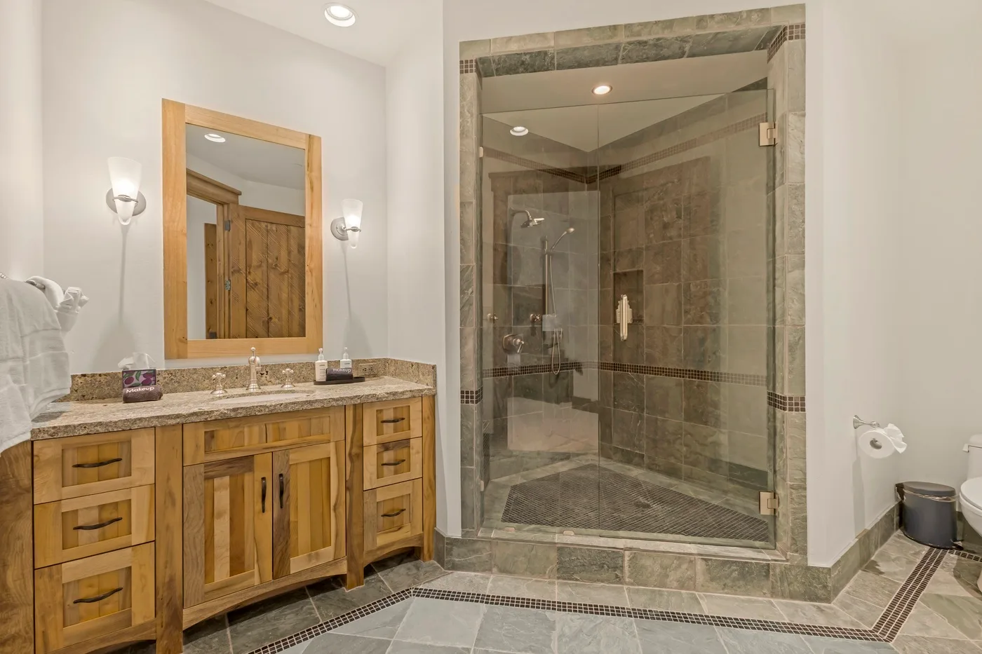 A bathroom with a wooden vanity, mirror, and glass-enclosed shower.
