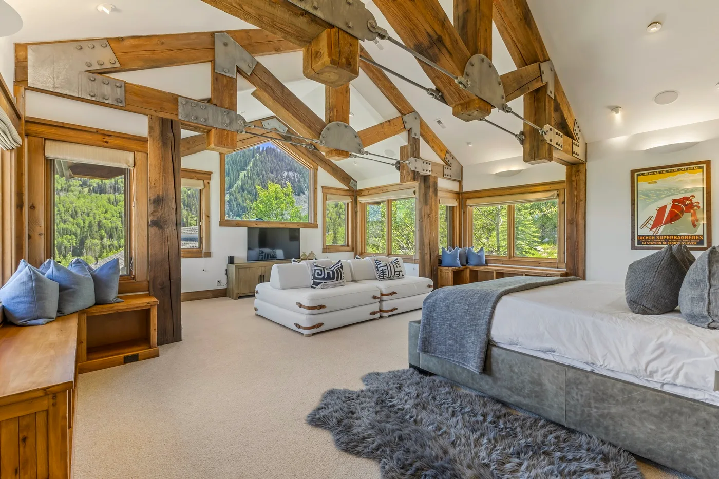 A bedroom with a bed, seating area, and large windows overlooking trees.