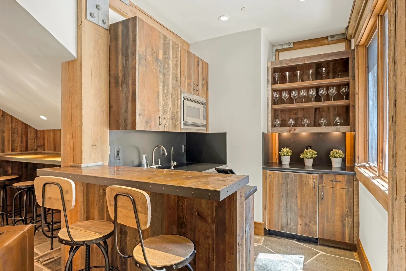 A wood-finished kitchen with a counter, bar seating, and glass-front shelving.