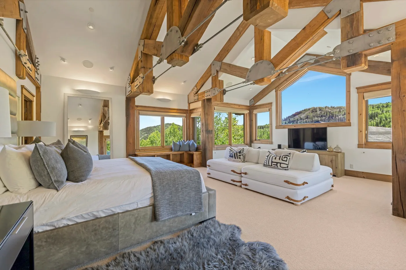 A spacious bedroom and sitting area with exposed wooden beams and large windows.