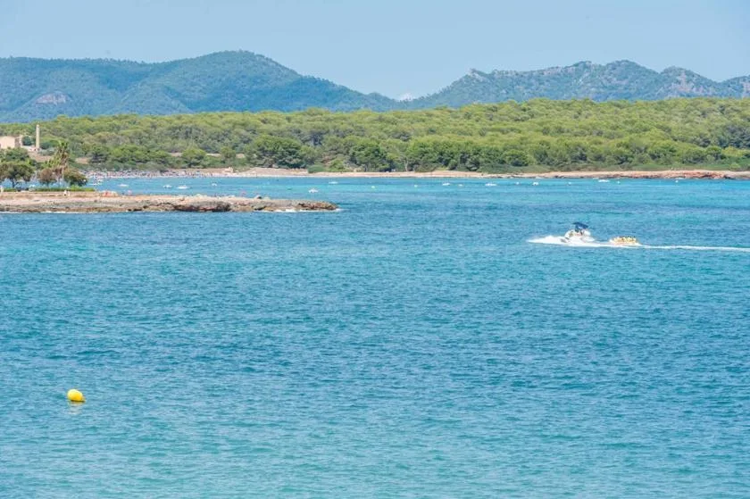 Turquoise water stretches toward a tree-lined shore and distant hills, with a small motorboat offshore.
