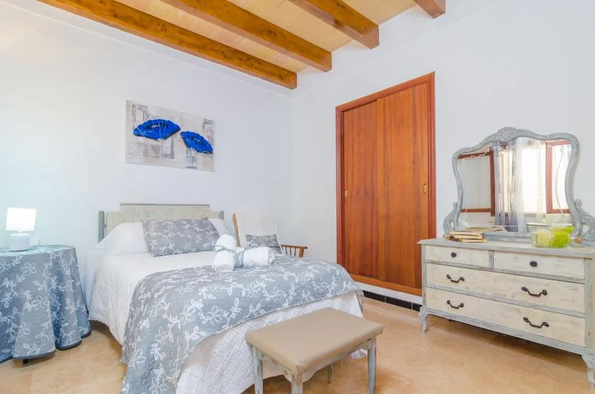 A bedroom with a bed, wooden ceiling beams, and a dresser with a mirror.