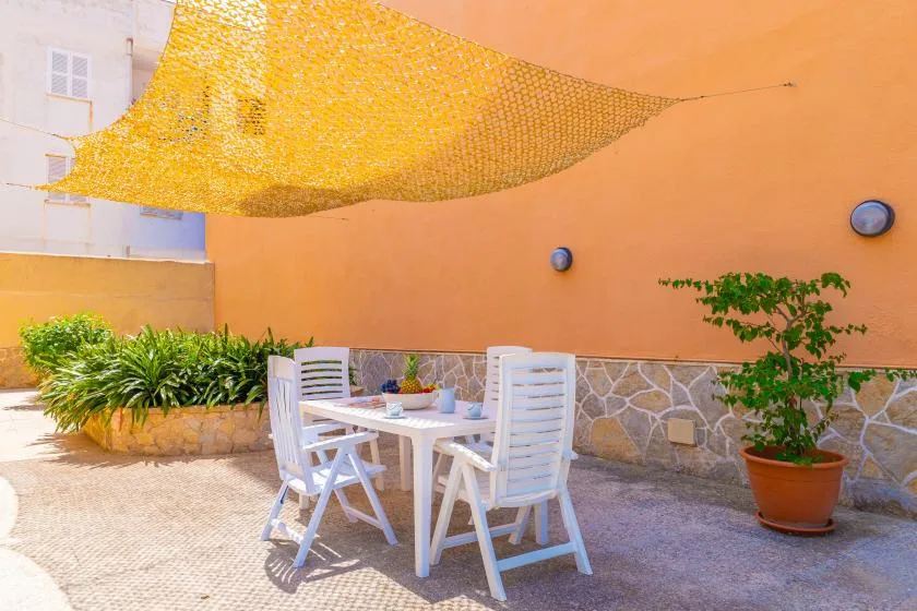 Un patio al aire libre con una mesa blanca y asientos bajo una cubierta de sombra.