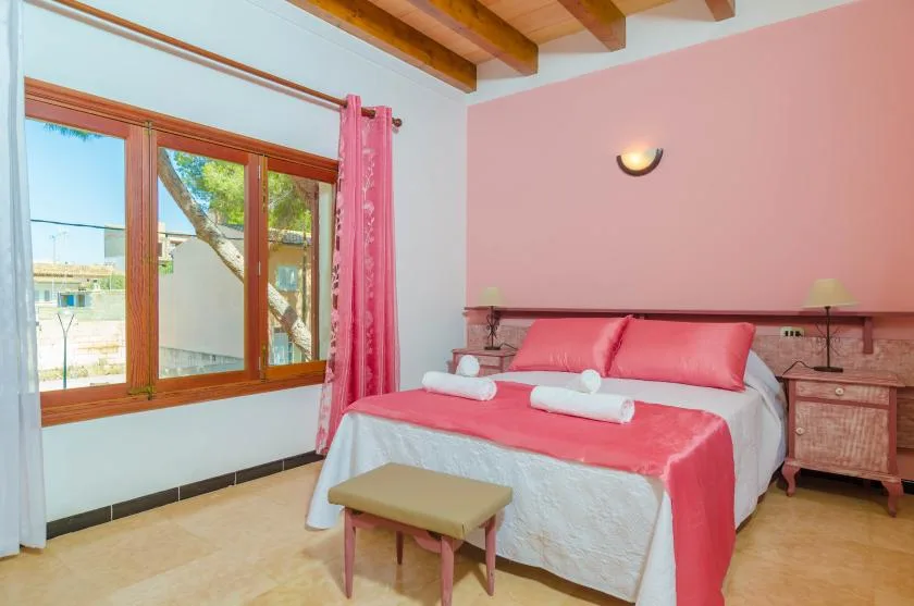 A bedroom with a bed dressed in pink bedding beside a large window.