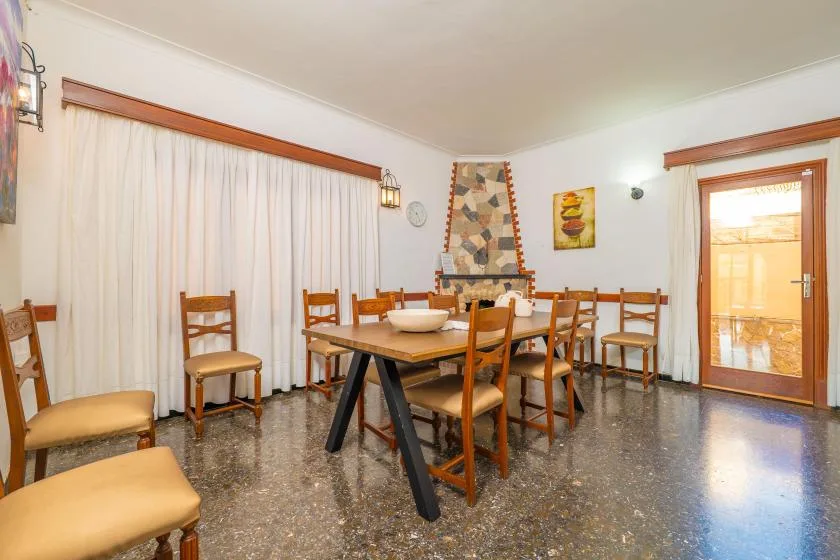 A dining room with a long wooden table, chairs, and curtained windows.