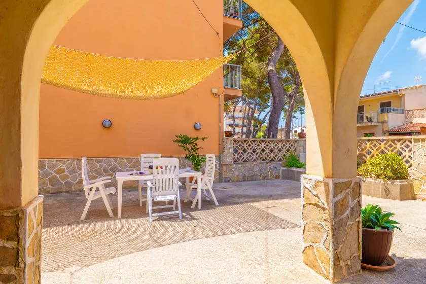 Un patio exterior sombreado con asientos blancos, muros de piedra y arcos.