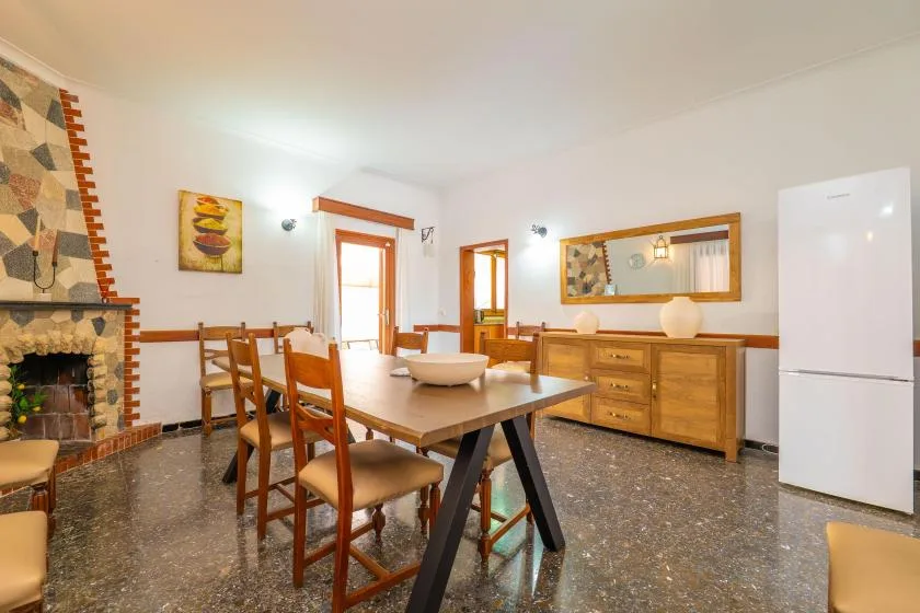 A dining area with a wooden table and chairs, a fireplace, and a refrigerator.
